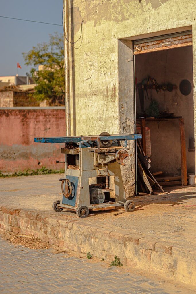 Old industrial saw machine in a sunny outdoor setting near a rustic workshop.